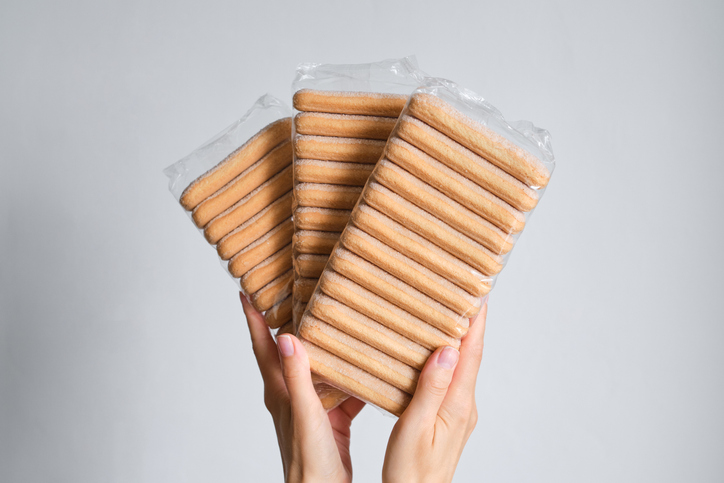 Cookies in a bundle close-up in the hands of a girl on a light background. Package with ladyfinger savoiardi cookies. Italian desserts. Transparent packaging for sweets
